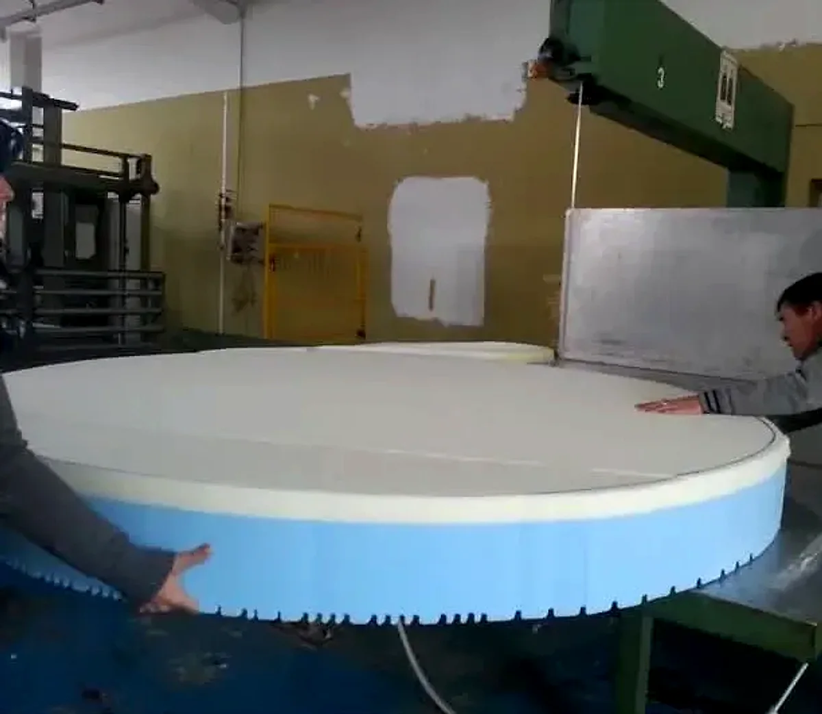 Due persone guidano un grande materasso rotondo durante il taglio sulla macchina